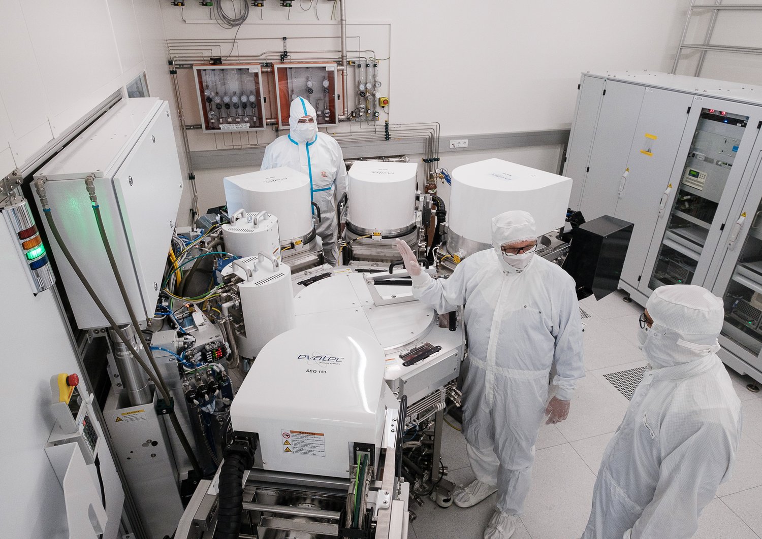 Several researchers standing in a clean room around a cluster tool