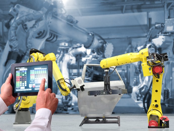 robots in a factory are being controlled by a person with a tablet