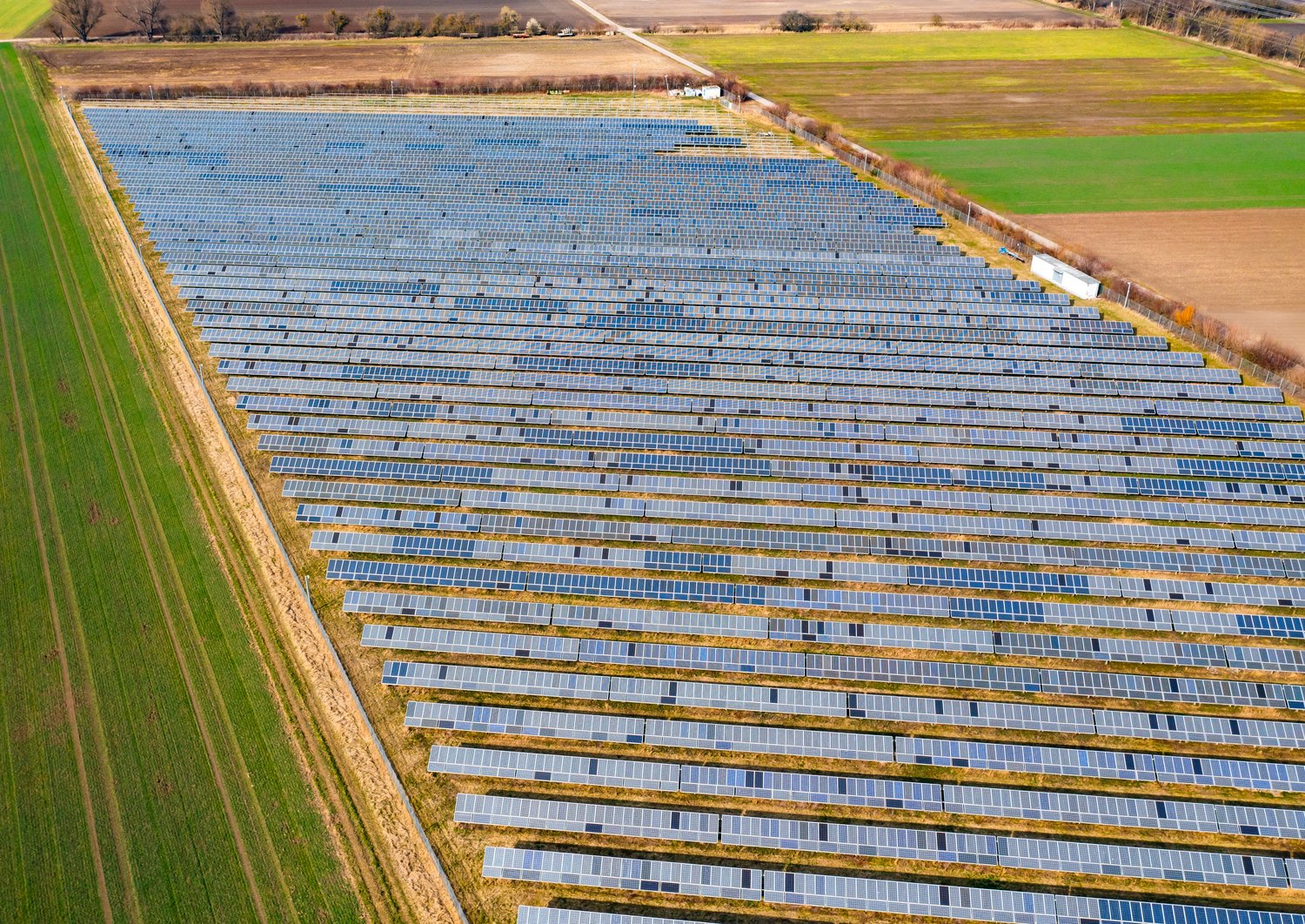 In the middle are slightly damaged PV systems. Surrounding the PV Systems there are yellow and green fields.