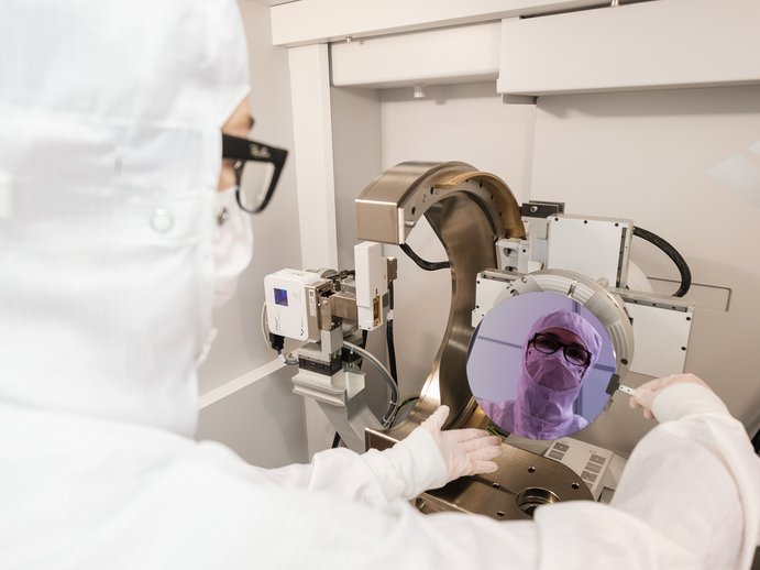 Madeleine in Schutzkleidung im Reinraum mit einem Wafer in der Hand. Ihr Gesicht spiegelt sich im Wafer. 