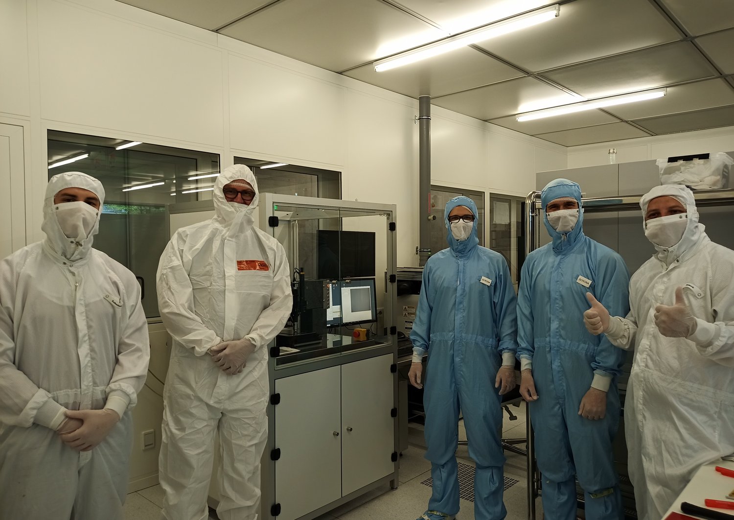 Five scientists in cleanroom clothing standing in a cleanroom 