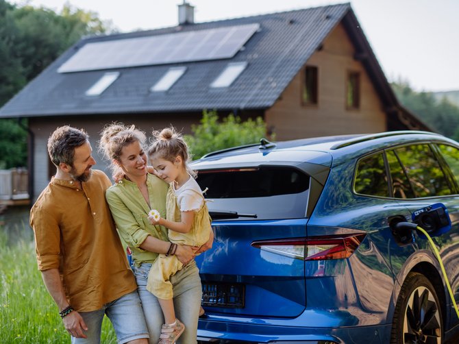 Familie steht im Garten vor einem Auto und einem Haus mit Solarpanelen