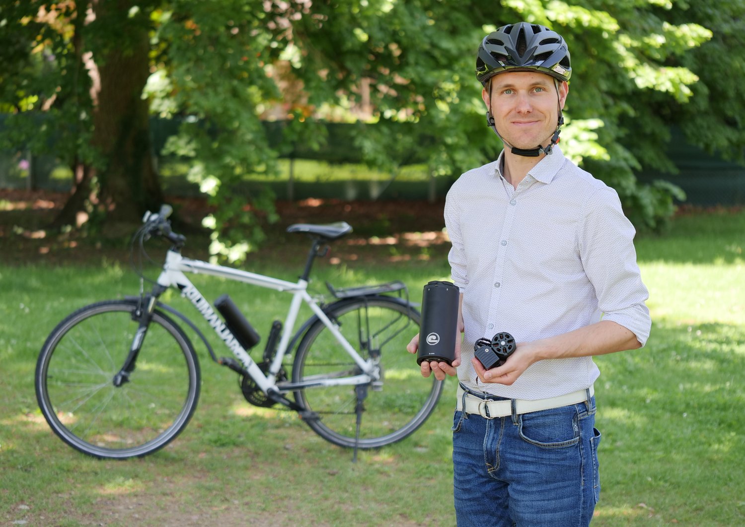 Herbert Hackl mit Fahrradhelm am Kopf und Fahrradbatterie in den Händen vor einem E-Bike