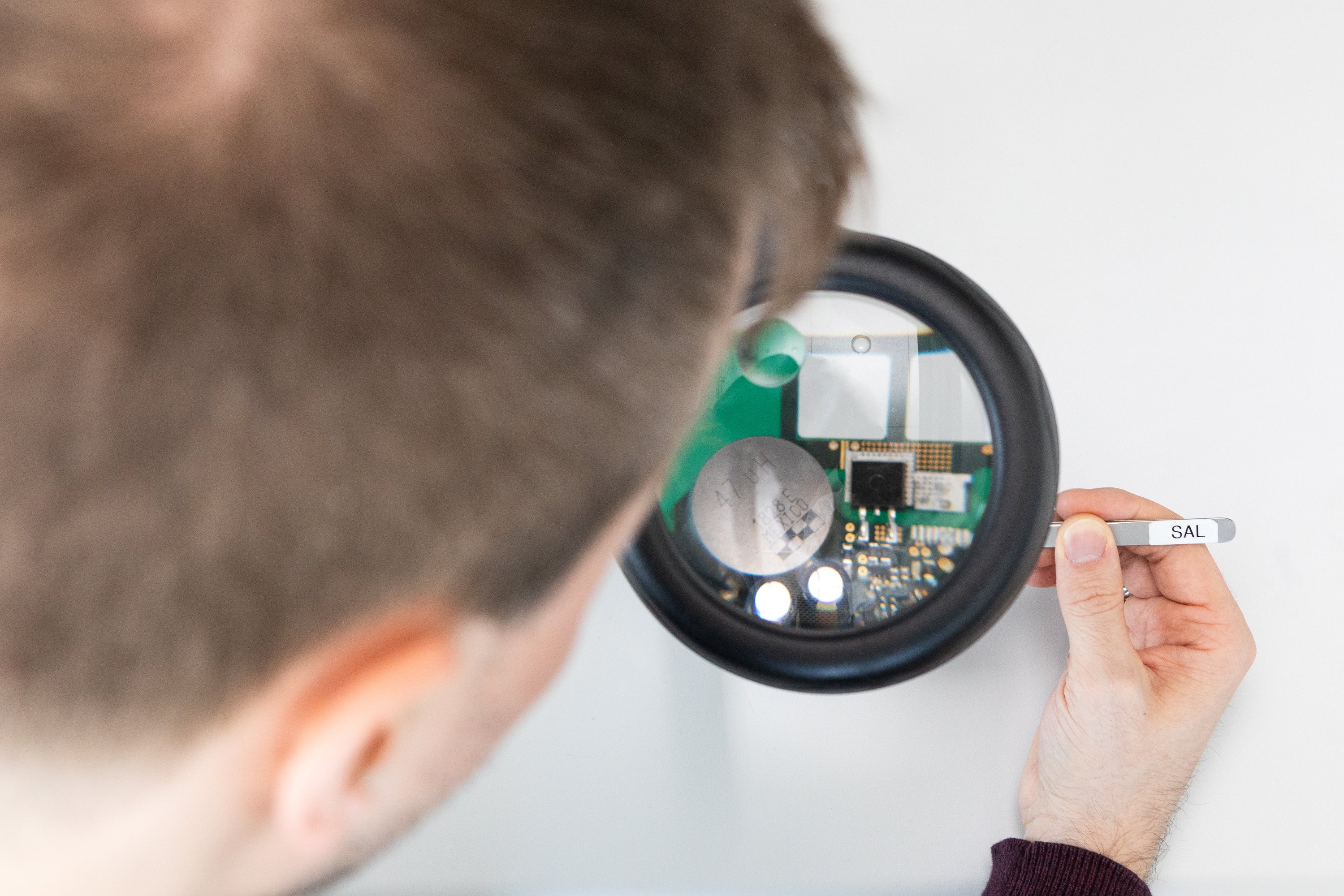 researcher is working on a printed circuit board, looking through a magnifying glass