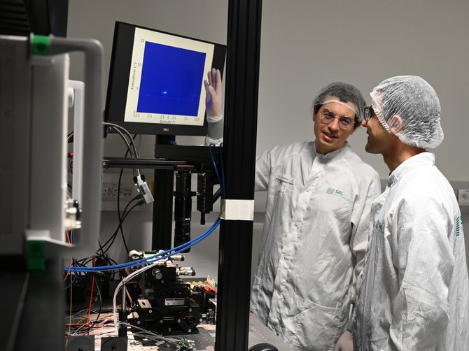 zwei Forscher in weißer Schutzkleidung stehen vor einem Computermonitor