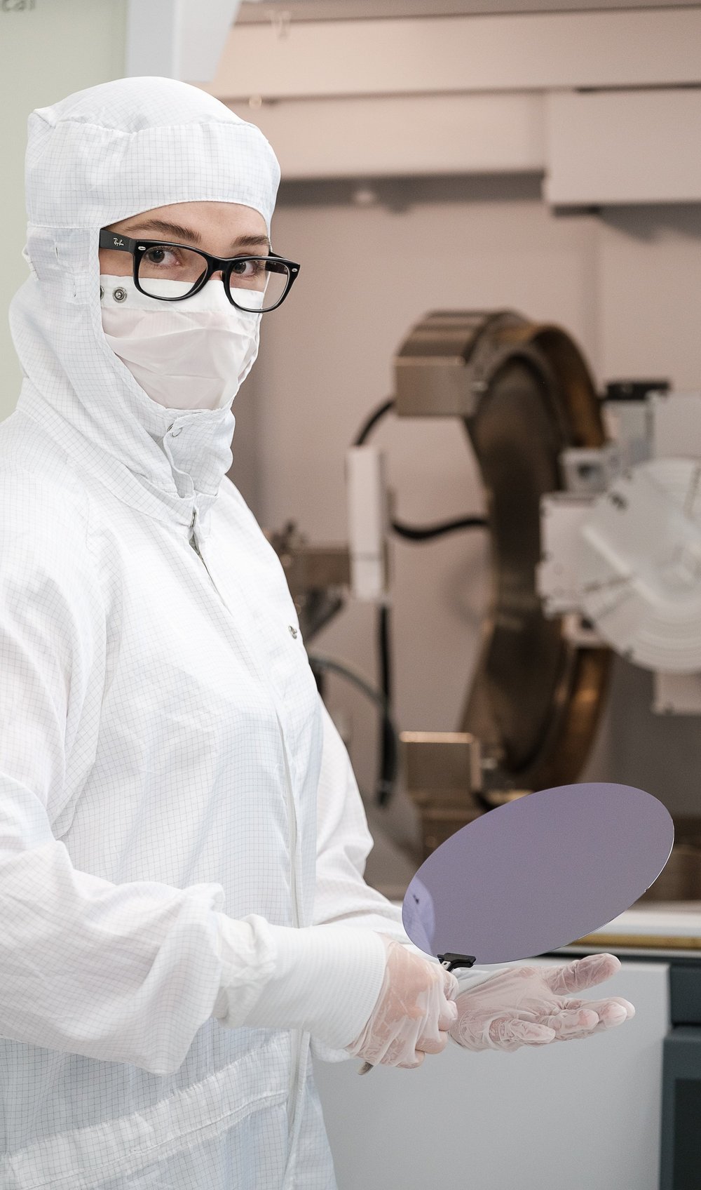 Madeleine in a protective suit and wearing gloves in the cleanroom. She holds a wafer.