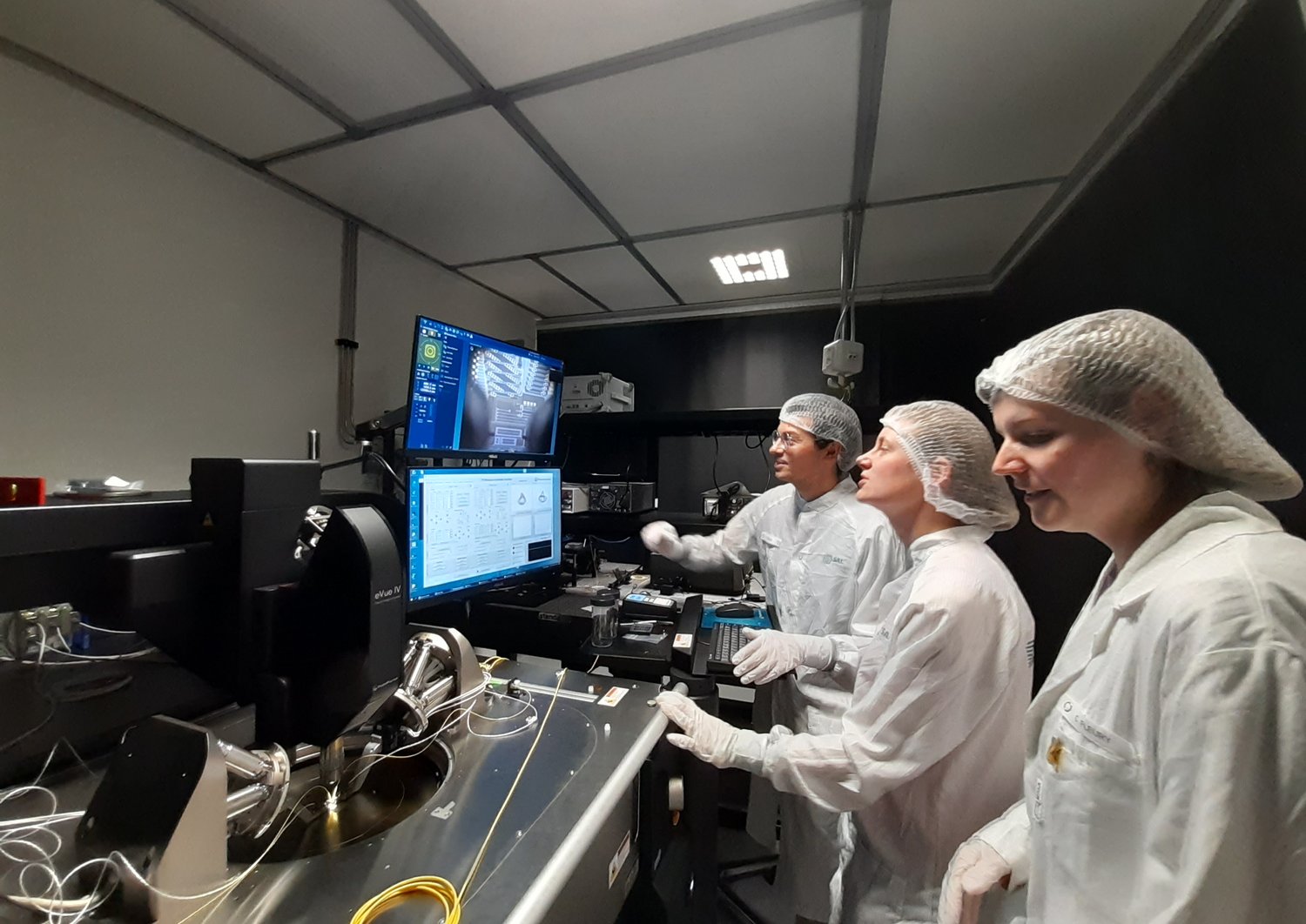 Drei Personen in Schutzkleidung blicken auf einen Computer