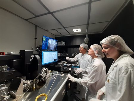 Three Scientists in lab clothing are looking at a computer