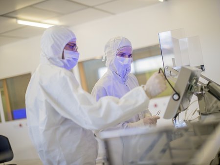 Zwei Personen die an etwas arbeiten in Laboranzügen in einem Reinraum