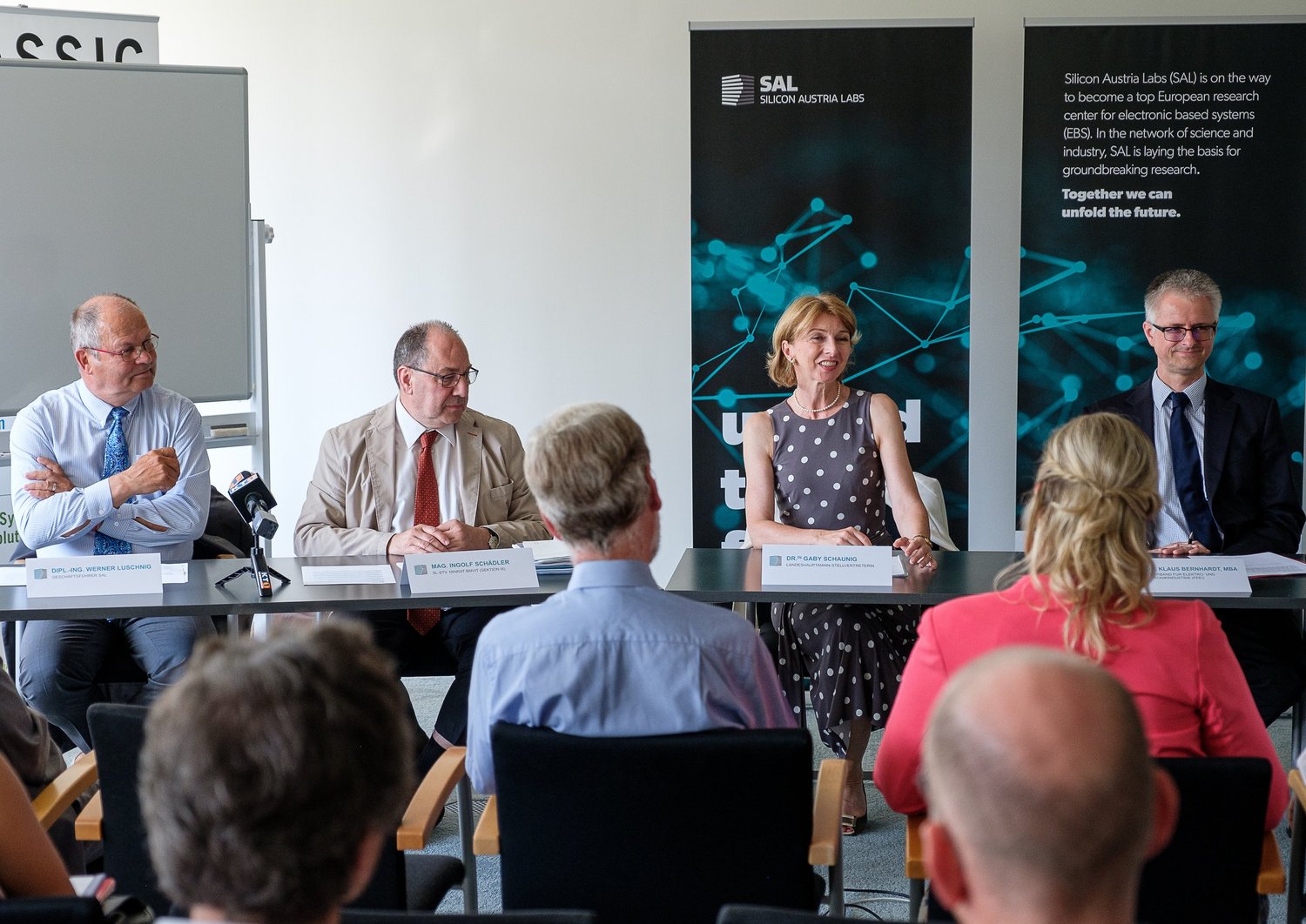 Four people talking at a press conference in front of an audience