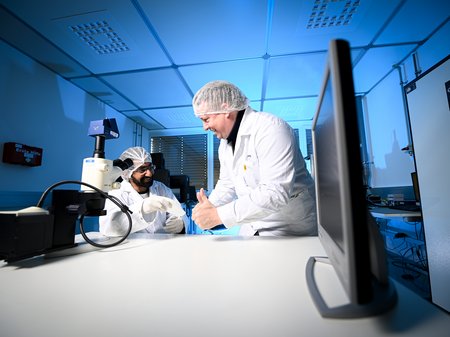 two researchers in protective clothing in the cleanroom in front of a measuring device